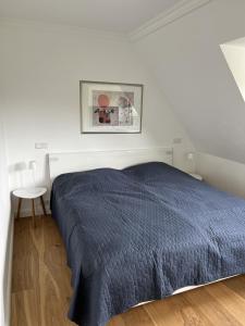 a white bedroom with a blue bed and a table at Schaumis Hus in Tinnum