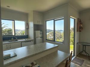 a kitchen with a counter and two large windows at Chenies Holiday Flat in Ngunguru