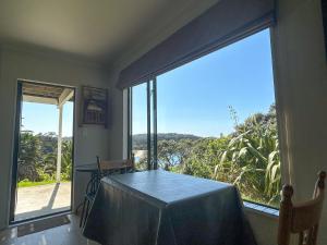 a dining room with a table and a large window at Chenies Holiday Flat in Ngunguru