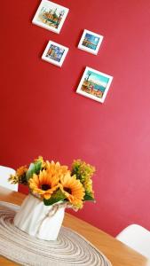 een vaas met bloemen op een tafel met foto's op een rode muur bij L'Incanto del Borgo Antico- Locazione Turistica in Bari