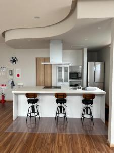 Una cocina con una encimera blanca y tres taburetes de bar. en Hakodate MOTOMACHI guesthouse, en Hakodate