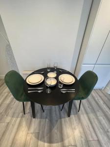 a black table with green chairs and plates and glasses at Seaforth Apartments 2 Bedroom Apartment with Parking and Garden by RockmanStays in Southend-on-Sea