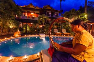 Ein Mann, der am Pool eines Resorts sitzt. in der Unterkunft The Hotel by the Red Canal in Mandalay