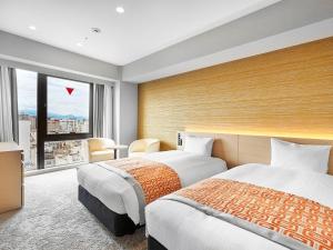 松山市にあるダイワロイネットホテル松山の大きな窓付きのホテルルームのベッド2台