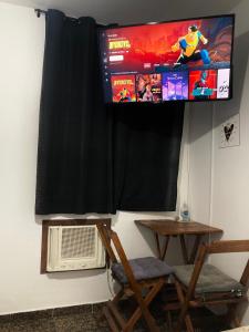 a tv hanging on a wall with a table and chairs at Suíte Trilha do Sol 2 in Arraial do Cabo