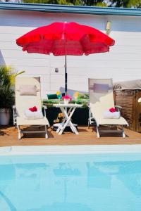 een tafel en twee stoelen met een rode parasol naast een zwembad bij Villa Terol, à proximité de l’océan in Saint-Paul