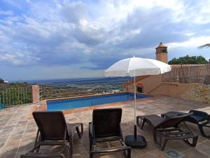 a patio with chairs and an umbrella and a pool at Casa Rural El Mirador in Vélez-Málaga