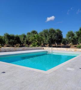 a swimming pool with blue water and trees in the background at Villa Dolce Far Niente Ostuni in Ostuni