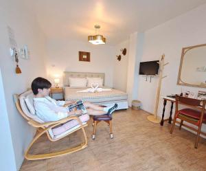 a boy sitting in a chair reading a book in a bedroom at Jamjuree Home at Udonthani in Udon Thani