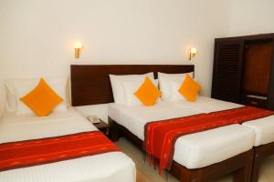 two beds in a hotel room with orange pillows at Gimanhala Hotel in Dambulla