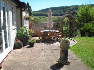 un patio con sombrilla, mesa y sillas en Hillside Cottage en Ledbury