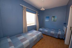 a blue room with two beds and a window at Pensión La Gaviota in Playa de Santiago