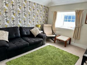 a living room with a black leather couch and a green rug at The Strontian Hotel in Strontian