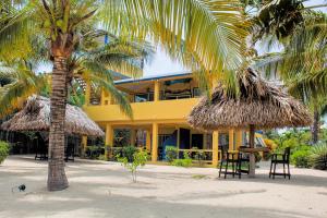 a yellow building with chairs and palm trees on the beach at Casa Palma Placencia in Placencia Village