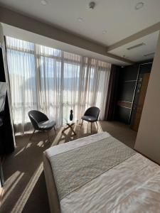 a bedroom with two chairs and a bed and windows at Hotel Sky Station in Tbilisi City