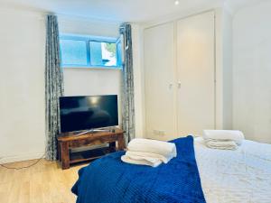 ein Schlafzimmer mit einem Bett mit einer blauen Decke und einem TV in der Unterkunft Sutton - Ground Floor Flat By The High Street in Sutton