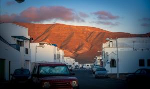 a street with a mountain in the background with cars at VolcanoKite Apartments in Famara