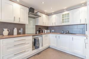 a white kitchen with white cabinets and a sink at Central Thames View 3BR by Sullivan Stays in London