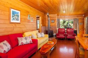 a living room with a red couch and red chairs at Sandy Bay Beachfront in Matapouri