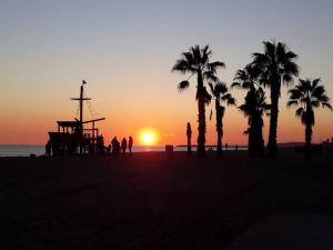 a sunset on a beach with palm trees and a ride at Apartamento acogedor in El Vendrell