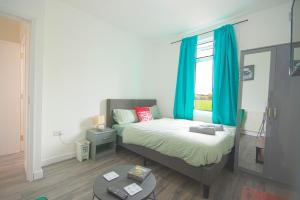 um quarto com uma cama com cortinas azuis e uma mesa em Cosy family home w/Wi-Fi, parking, self check-in em Londres