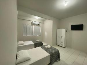 a small room with two beds and a refrigerator at Infinit Hotel Flats in Janaúba