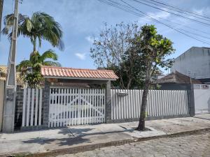 a white fence with a gate and a palm tree at Casa 50m do mar in Matinhos