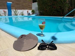 um chapéu e óculos de sol e um copo de vinho ao lado de uma piscina em Casa Paraiso de Sonho Verde em Paripueira