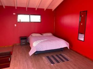 ein Schlafzimmer mit einem Bett in einer roten Wand in der Unterkunft Departamentos altos de yelqui in Puqueldón