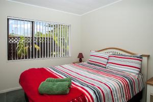 a bedroom with a bed with a red blanket and a window at Denby Crest in Whangarei