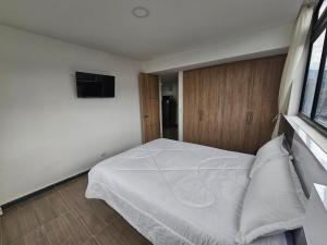 Schlafzimmer mit einem weißen Bett und einem TV in der Unterkunft Apartamento Meredi in Bogotá