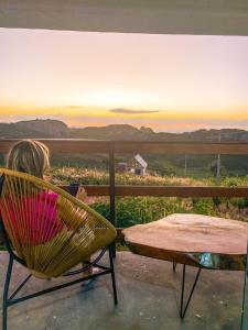 Ein kleines Mädchen, das auf einem Stuhl sitzt und den Sonnenuntergang sieht. in der Unterkunft Entre Serras Gastropub e Chalés in Monte das Gameleiras