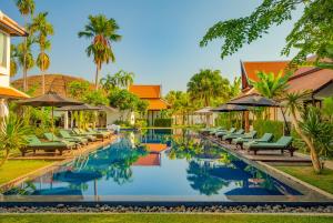 una imagen de una piscina del complejo con sillas y sombrillas en The Embassy Angkor Resort & Spa, en Siem Reap