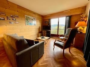 ein Wohnzimmer mit einem Sofa, Stühlen und einem Fenster in der Unterkunft Les Xettes, bel appartement style chalet avec vue in Gérardmer