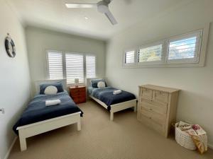 a bedroom with two beds and a dresser and windows at Sea Breeze on Carroll - 4BR beachside home in Mollymook