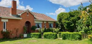 a red brick house with bushes and trees at Terracotta Cottage in Te Awamutu