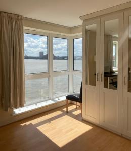 Zimmer mit einem großen Fenster mit einem Stuhl und einem Schreibtisch. in der Unterkunft Very large ensuite room with wonderful view over the river Thames in a peaceful & calm residential building - SHARED flat with 1 host in London