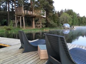 a deck with two chairs and a tree house on the water at Treehouse Čiekurs in Duķuri