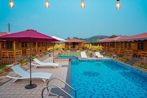 a pool at a resort with chairs and umbrellas at Grace Exotica Goa in Canaguinim