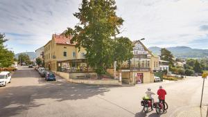 two people riding bikes down a street in a town at Wellness Hotel Kocanda in Děčín
