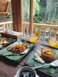 two plates of food on a table with orange juice at Aksha Riverside Ubud in Tampaksiring