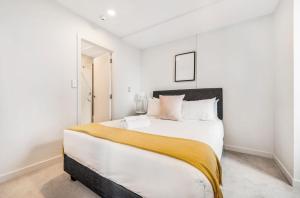 a white bedroom with a large bed with a yellow blanket at Skytower view and Seaview 2 bedroom Apartment in Auckland