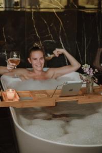 uma mulher numa banheira com um computador portátil e um copo de vinho em VIBE LUXURY CABINS em Arnuero