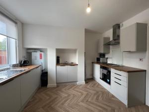 a kitchen with white cabinets and a wooden floor at Cosy Fresh New Refurbished House in Doncaster