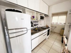 eine weiße Küche mit einem Kühlschrank und einer Spüle in der Unterkunft Confortável apartamento perto de praias - Bertioga in Bertioga