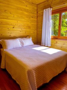Ce lit se trouve dans une chambre en bois dotée d'une fenêtre. dans l'établissement Chalé Vale das Pedras, à Praia Grande