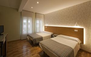 Una habitación de hotel con dos camas y un televisor. en Hostal Bezana, en Burgos