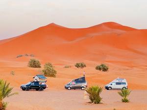 een groep voertuigen geparkeerd in de woestijn bij Hotel Camping Les Roses Des Dunes in Merzouga