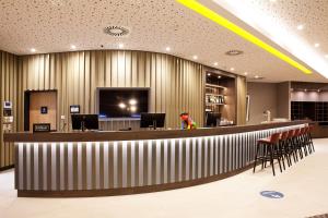 a lobby with a bar with chairs and a tv at Hampton by Hilton Munich Airport South in Hallbergmoos