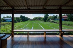 a porch with benches and a field in the background at Suk Sabai Homestay in Sukhothai